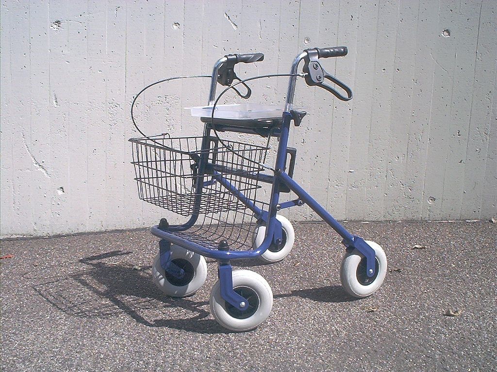 A picture of a blue framed rollator with a black basket. It has four white wheels and a seat above and behind the basket.