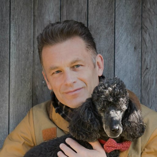 A smiling Chris, holding one of his Poodle dogs in his arms.