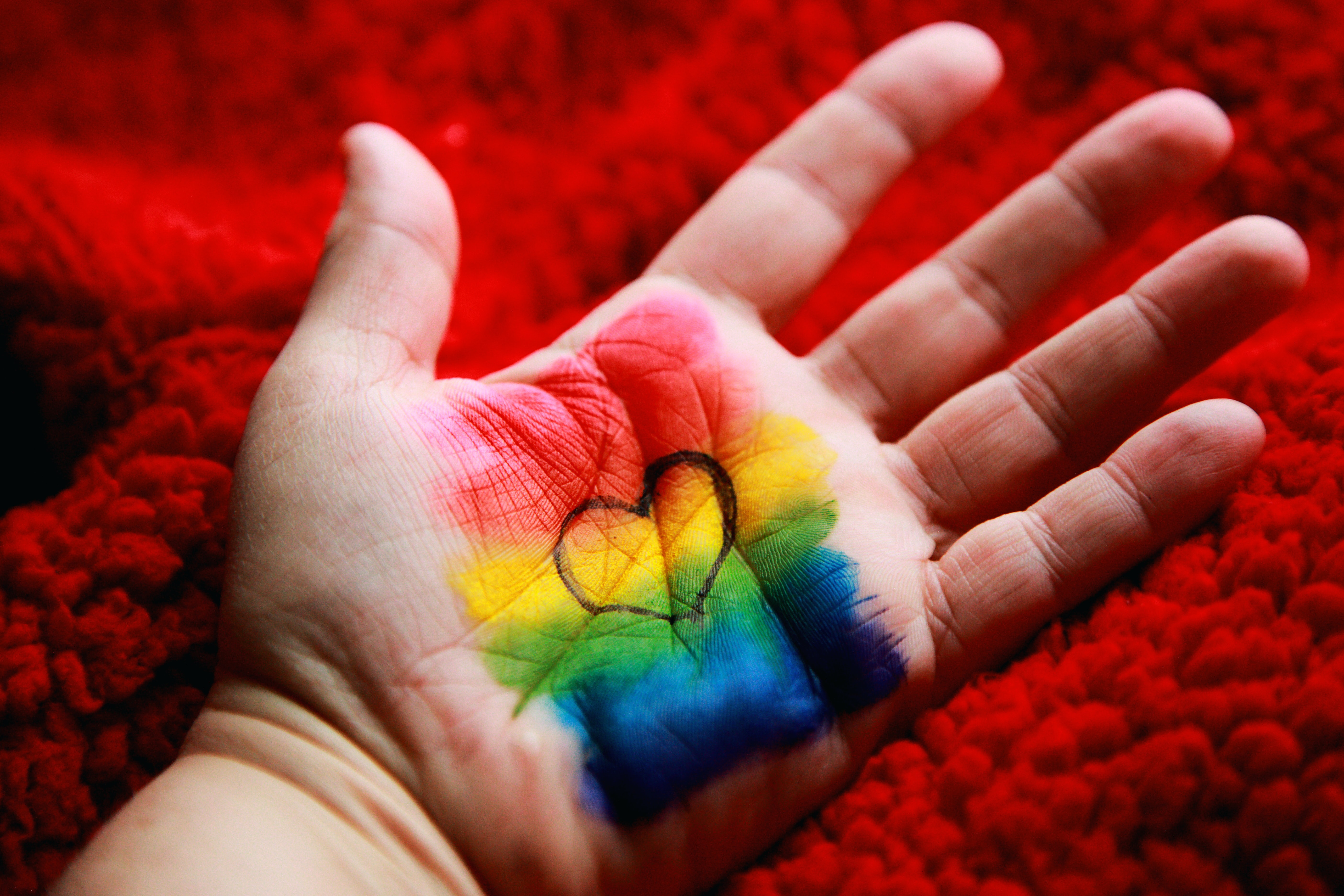 Close up of a palm with the LGBT+ rainbow flag painted on it with a heart drawn in black biro on top of it.