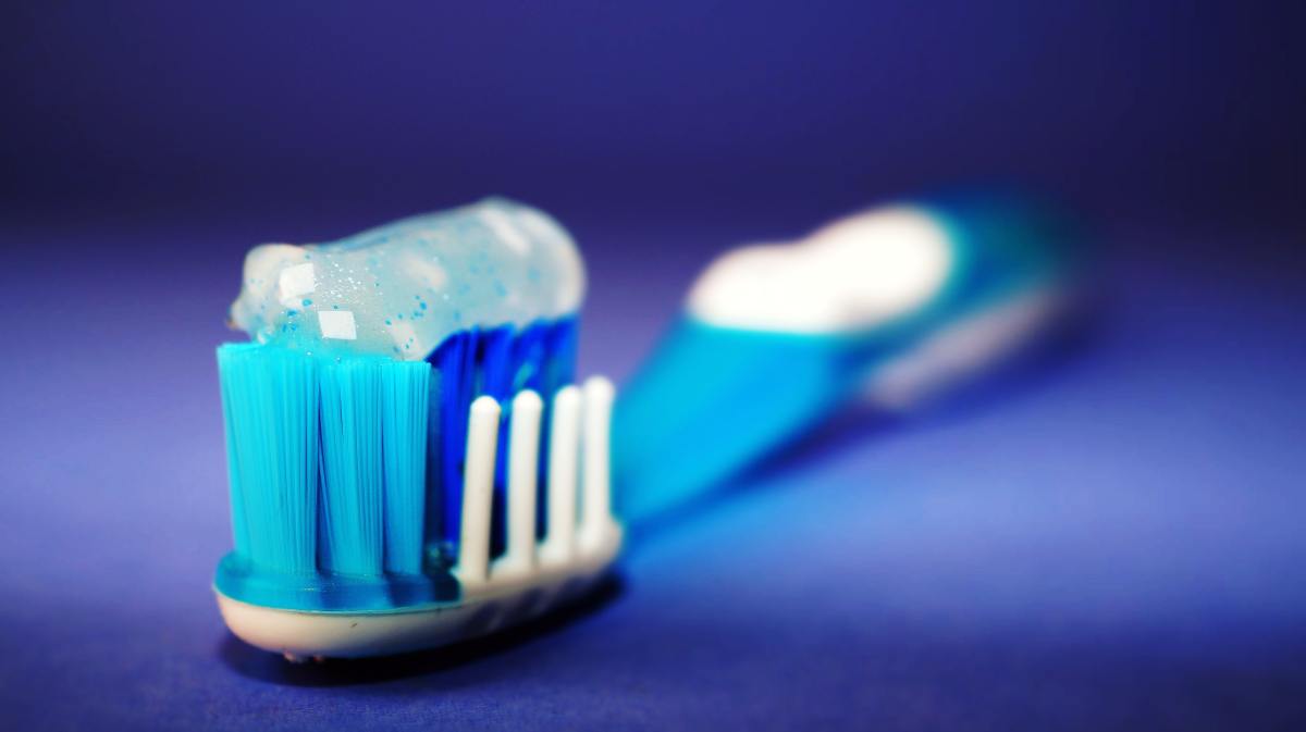 A blue toothbrush on a blue background with toothpaste on the bristles.