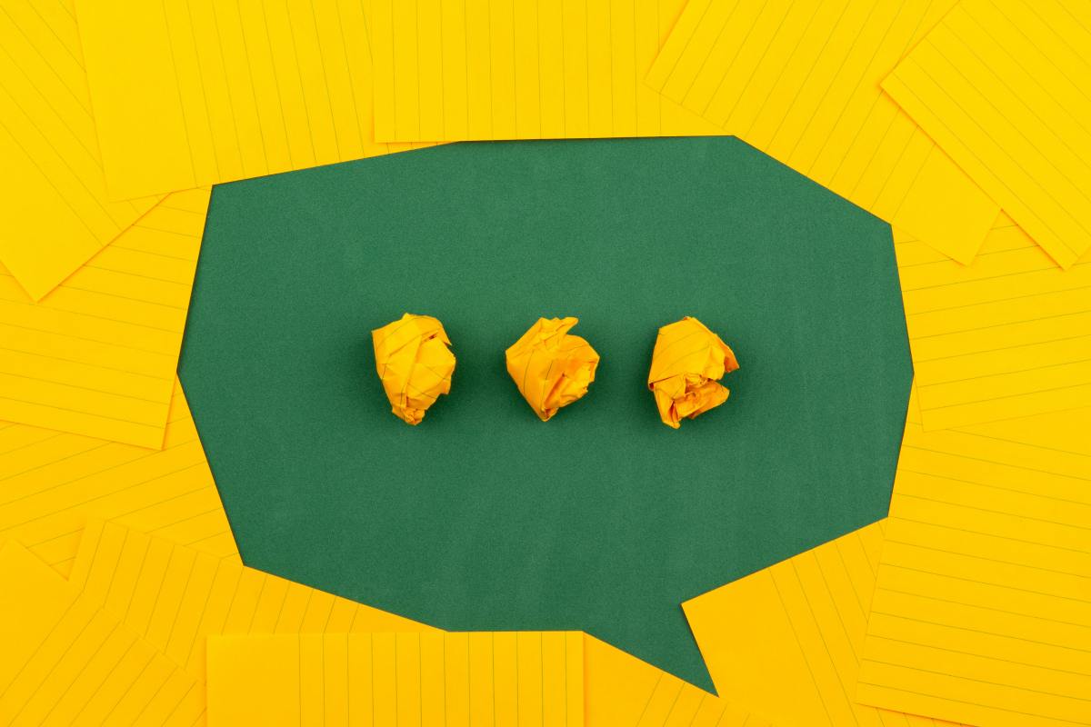 A green speech bubble made with yellow lined paper on top of plain green paper. three rolled up bit of yellow paper in the middle of the speech bubble