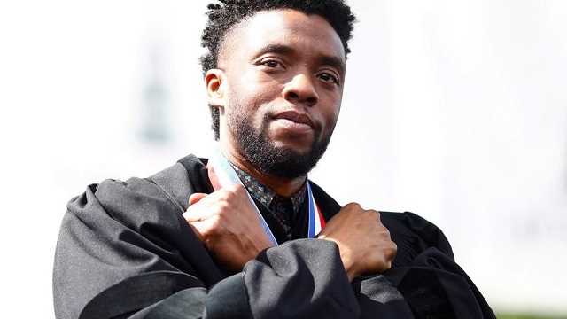 Chadwick Boseman is wearing a black coat with a medal on him while he is doing his famous "Wakanda Forever" pose from the Marvel Movie Black Panther. 